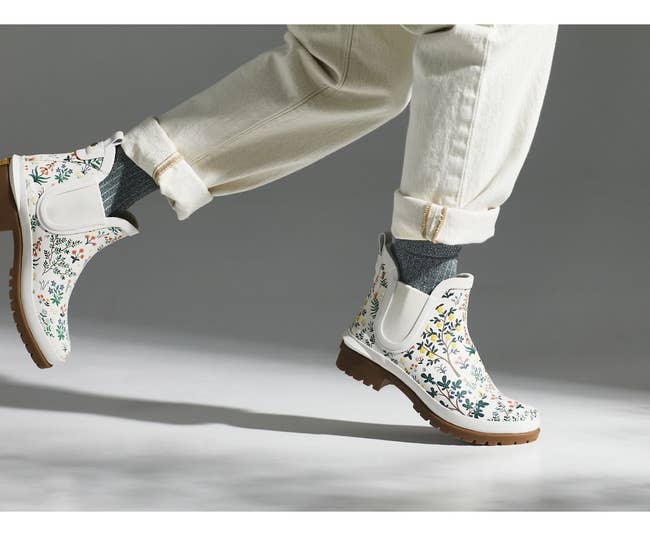 a model in white rain booties with a floral pattern on them