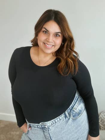 reviewer smiling, wearing a long-sleeve achromatic  apical  tucked into high-waisted jeans