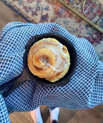 reviewer holding a black skillet with a cinnamon roll in it 