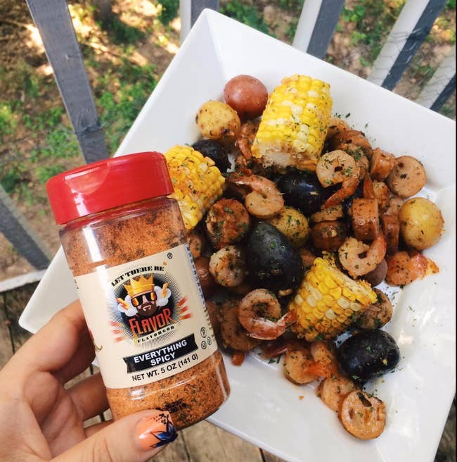 shrimp boil covered in orange everything spicy seasoning being held by a reviewer's hand 