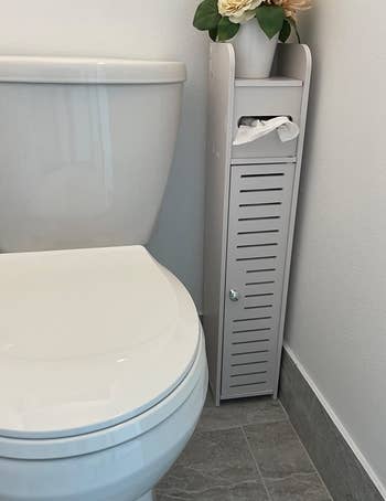reviewer photo of the white storage cabinet in a corner of their bathroom next to the toilet with its door closed