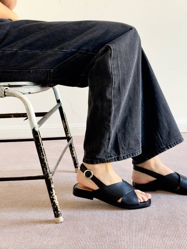 Person seated connected  a chair, wearing wide-leg pants and achromatic  sandals with a buckle