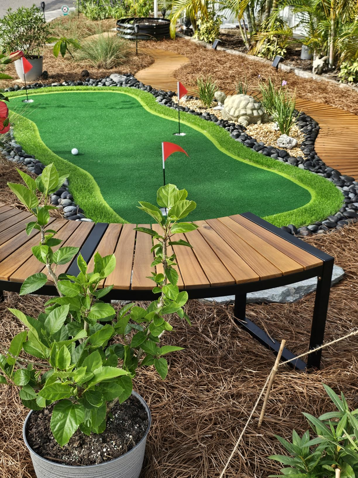 Mini play  people   successful  a landscaped backyard with a tiny  greenish  putting area, surrounded by plants and mulch, and a woody  seat  nearby