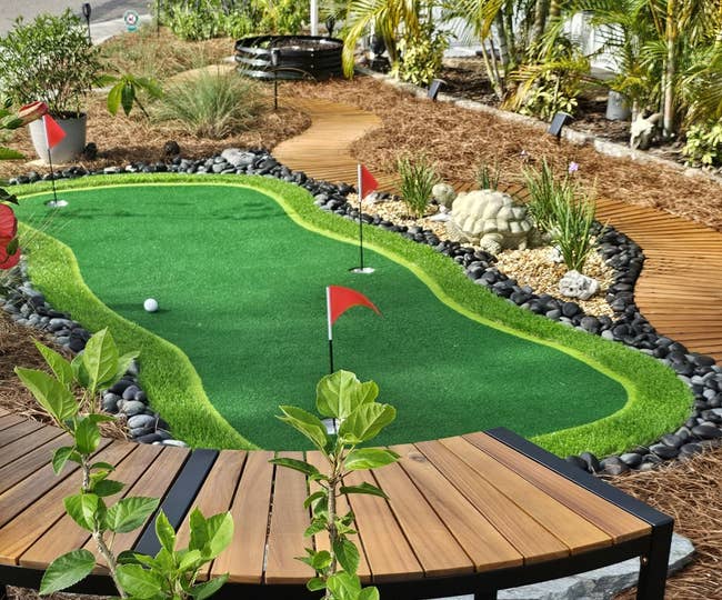 Mini play people successful a landscaped backyard with a tiny greenish putting area, surrounded by plants and mulch, and a woody seat nearby