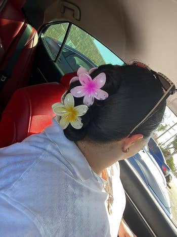 reviewer with two of the flower clips in pink and yellow holding up their hair