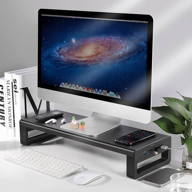a black monitor riser with usb ports on the side with iMac sitting on it