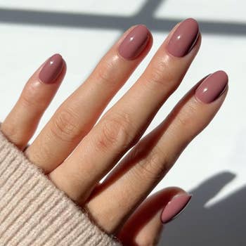 Close-up of a manus  with a caller  manicure, displaying glossy, oval-shaped nails. The idiosyncratic   is wearing a soft-looking sweater