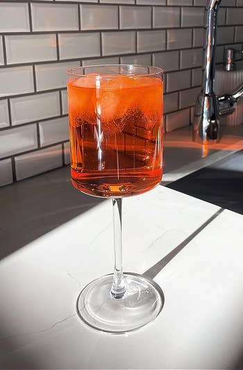 The glass filled with a bright orange drink on the counter with sunlight shining on it