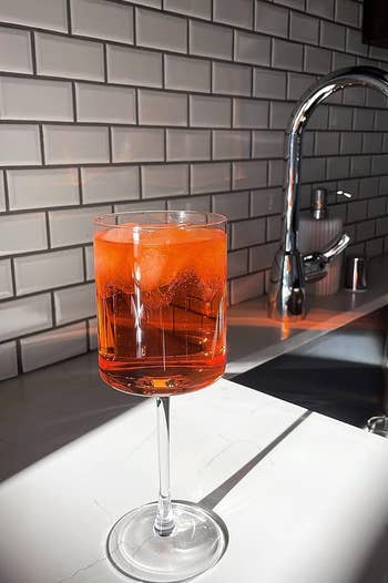 The glass filled with a bright orange drink on the counter with sunlight shining on it