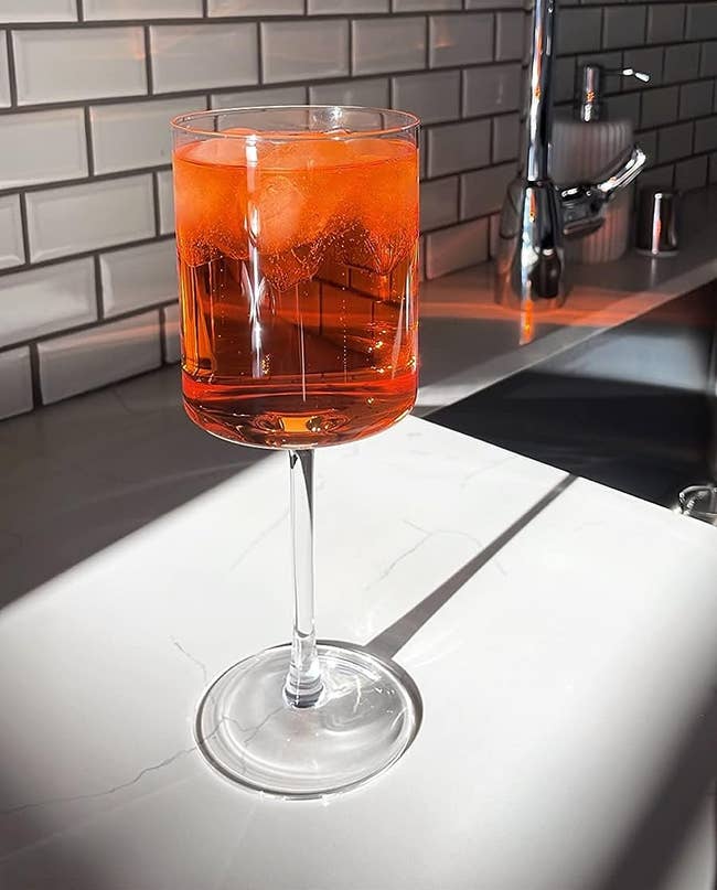 The glass filled with a bright orange drink on the counter with sunlight shining on it