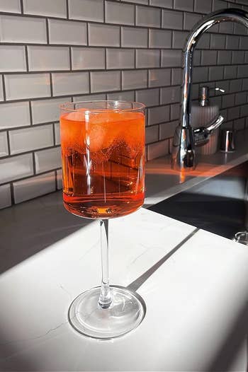 The glass filled with a bright orange drink on the counter with sunlight shining on it