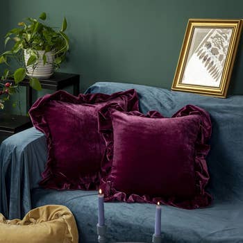 Two plush velvet pillows on a bed with a framed picture and candlesticks nearby, for home decor inspiration