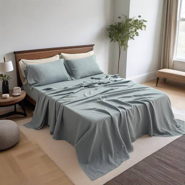 A neatly made bed with soft linens and pillows, set in a stylish bedroom with a nightstand and a plant, basked in natural light