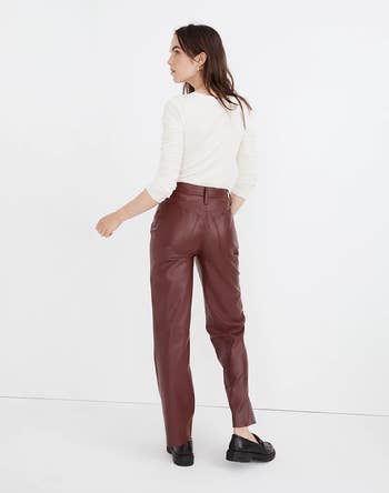back of a model wearing brown faux leather pants with a white sweater