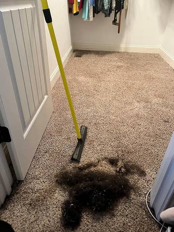 A pile of swept-up hair on a carpeted floor next to a yellow broom