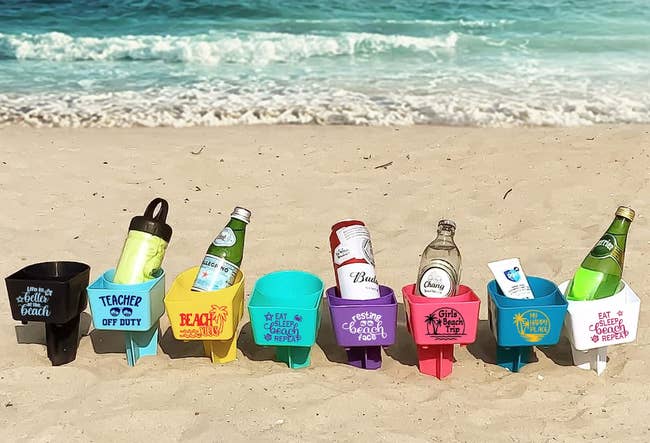 Assorted beverage holders with fun quotes lined up on a sandy beach