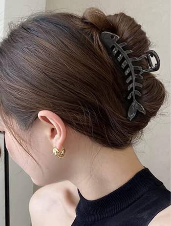 Model with a black fishbone shaped claw clip holding their hair in a bun 