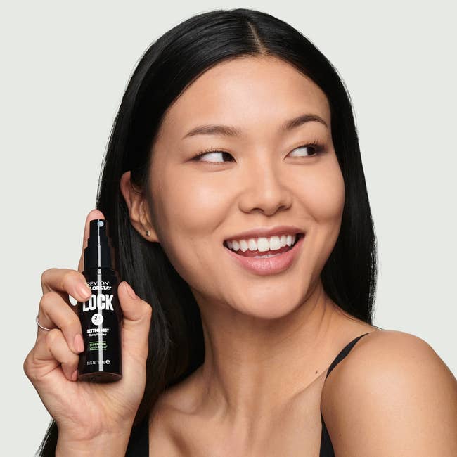 Person smiling, holding a skincare product bottle, suggesting excitement and satisfaction with the item