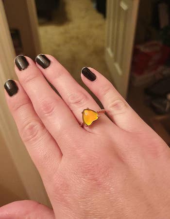 Hand with black nail polish showcasing a ring with an orange gemstone shaped like a flower