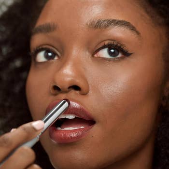 A person applying lipstick to their lips, focusing on the makeup product