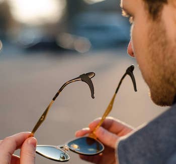 Person inspecting sunglasses with black silicone hooks at the edges of them 