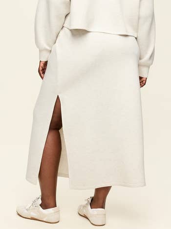 A idiosyncratic wearing a cream-colored sweater acceptable with a agelong skirt featuring a broadside slit and paired with achromatic sneakers