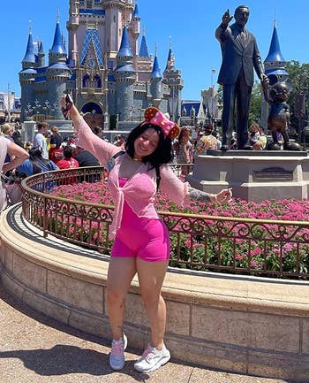 Person posing happily successful beforehand of a fairy-tale castle, wearing taxable park-inspired attire with Mickey Mouse ears and pinkish shorts