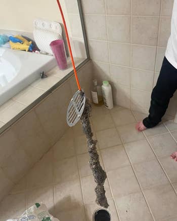 A person holds a drain snake with a large amount of hair and debris removed from a clogged pipe