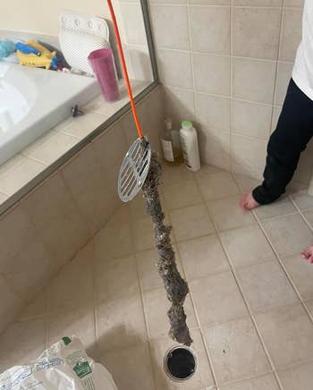 A person holds a drain snake with a large amount of hair and debris removed from a clogged pipe