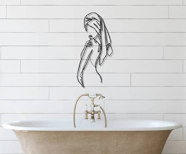 the black metal line wall art of a person's silhouette hanging above a bathtub