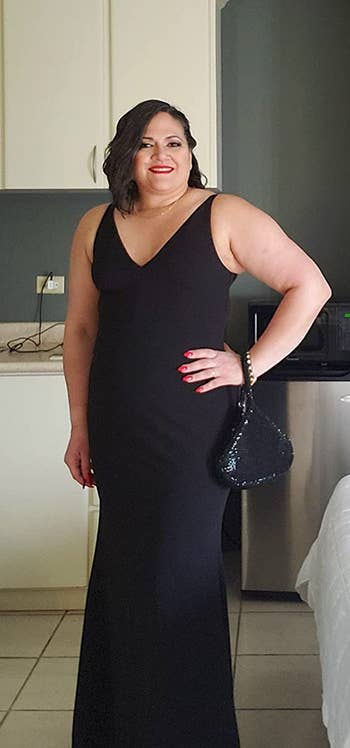 Reviewer wearing maxi sleeveless black dress with V-neckline and mermaid bottom in front of white cabinets