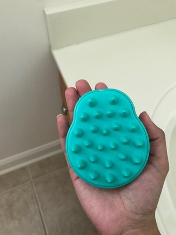 reviewer holding the shampoo scalp brush in teal