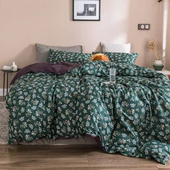 a dark green floral duvet set on a bed folded over slightly, revealing the dark purple on the other side