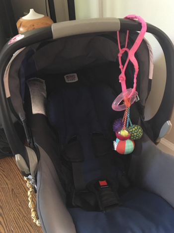 reviewer using cup catcher to keep a baby toy on their car seat 