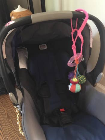 reviewer using cup catcher to keep a baby toy on their car seat 