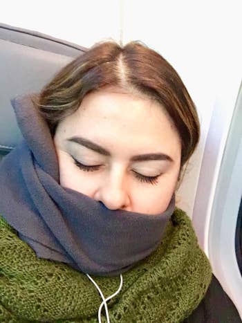 reviewer wearing the same neck pillow in a dark gray color on a flight