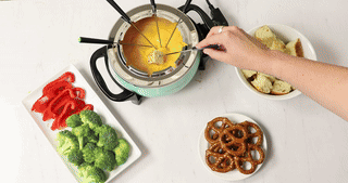 A manus dips breadstuff into a fondue cookware filled with food and past a strawberry successful cocoa