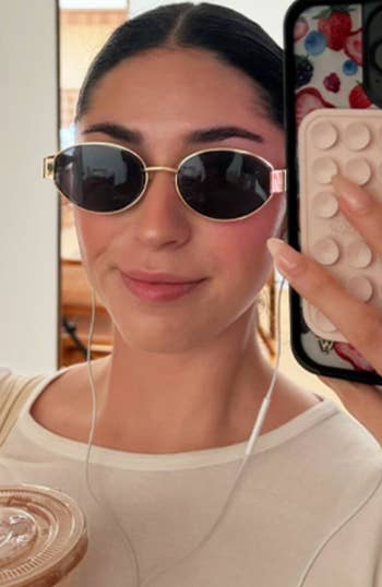 Person takes a selfie holding a smoothie and wearing stylish sunglasses with earbuds. Phone lawsuit  has a popular  socket. Perfect for a casual, trendy look