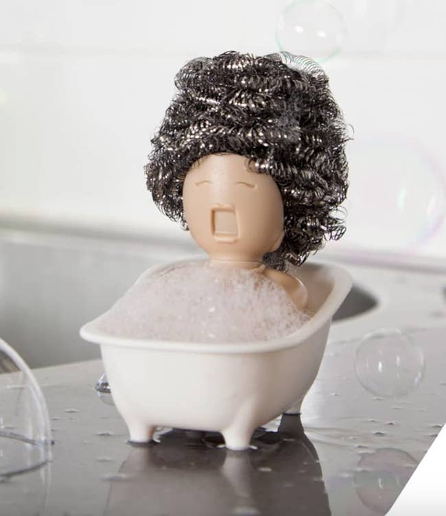 Novel soap holder shaped like a person in a bathtub with a curly hair scrubber. Fun addition to bathroom decor