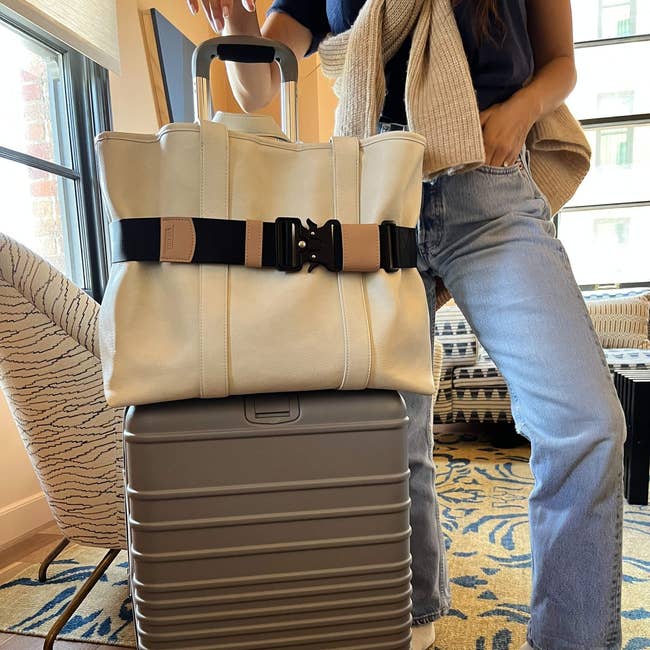 a model standing with their suitcase with a cincha belt securing a tote bag to the top of it 