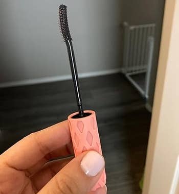 Hand holding a pinkish rubber-grip mascara wand with a curved brushwood successful a location setting
