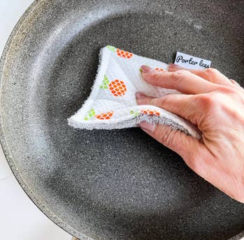 hand using the orange-print sponge to clean a pan