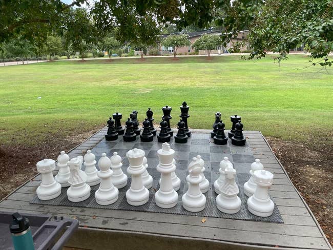 Outdoor chessboard with life-size black and white chess pieces set up for a game in a park