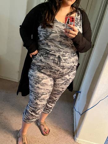 reviewer in camo jumpsuit with black cardigan over it