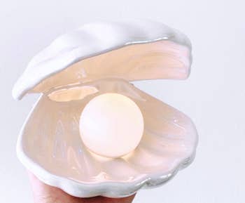 Hand holding an open shell with a pearl-shaped lightbulb inside