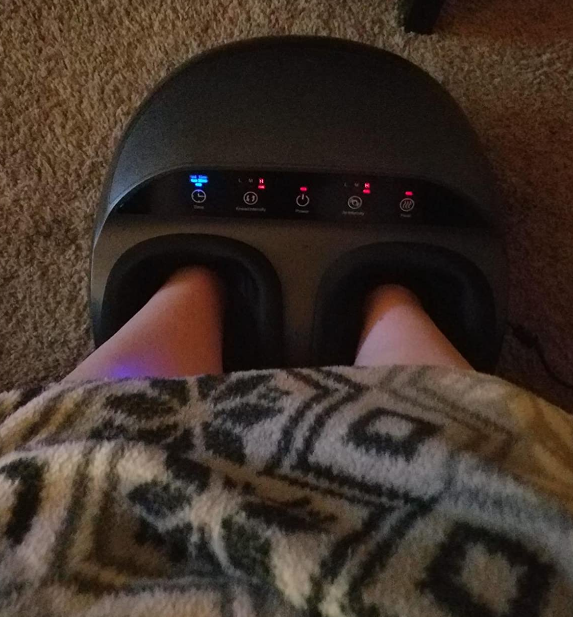overhead shot of reviewer's legs wrapped up in a blanket while they use the foot massager