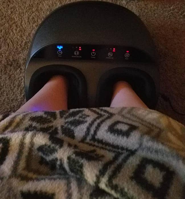 overhead shot of reviewer's legs wrapped up in a blanket while they use the foot massager