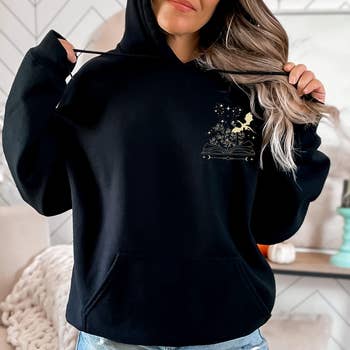Model models a achromatic  hoodie with a subtle prima  and works  design, pairing it with casual denim shorts, suitable for a relaxed buying  style