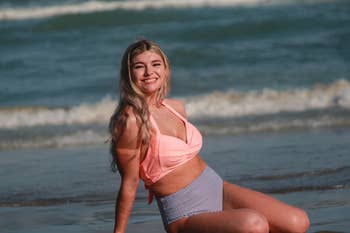 Woman in a pink bikini top and striped bottoms sitting on the beach