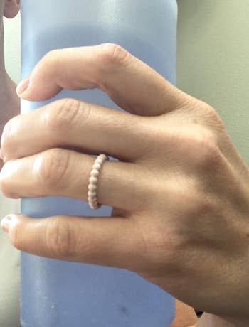 Hand holding a ample  bottle, wearing a elemental  beaded ring, suggesting hydration arsenic  portion  of a buying  manner  choice